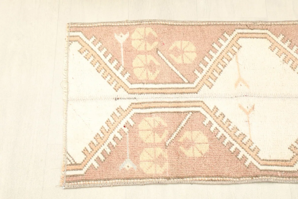 Overhead view showing one end of the rug with its geometric and tribal designs in rose, ivory, and tan.