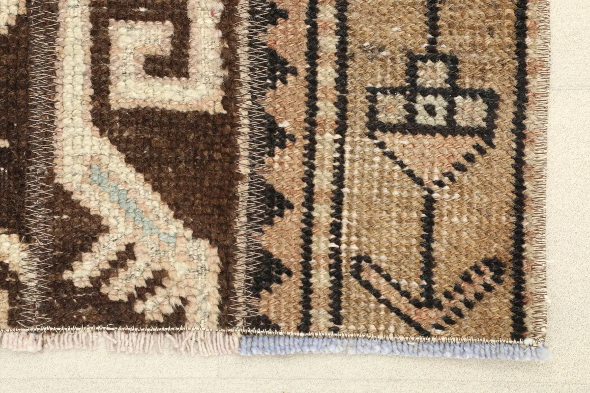 Close-up detail of the rug's pattern, showing brown and tan wool pile with ivory and rose geometric motifs.