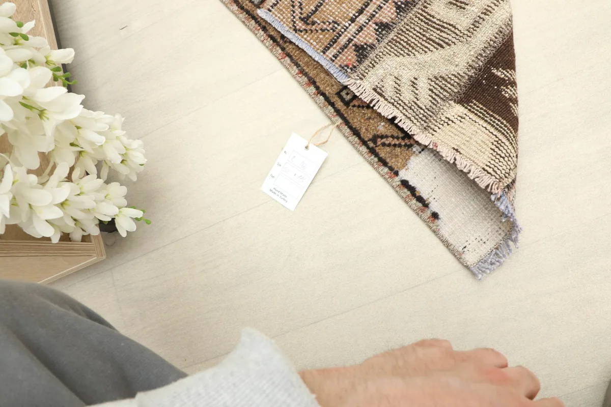 Corner of the rug with a tag, demonstrating its size and scale next to a person's arm.