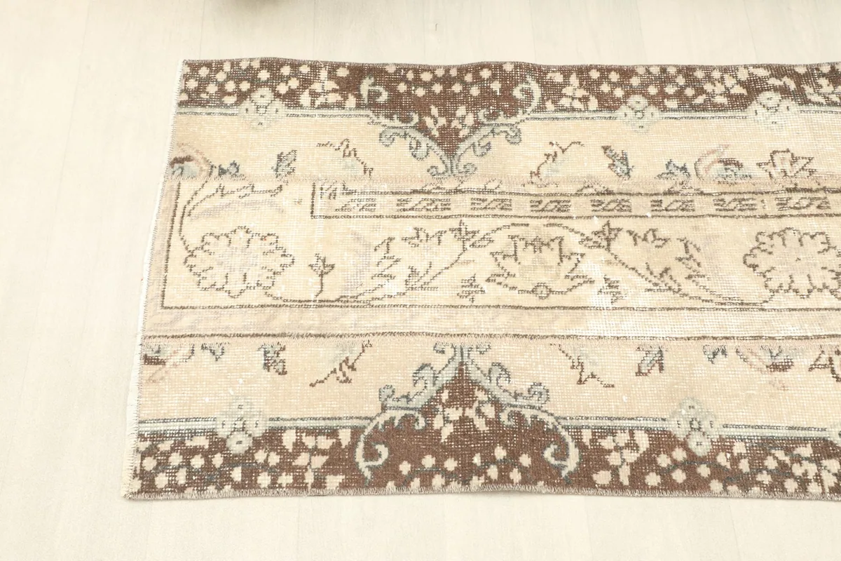 Angled view of one end of the rug, showing the beige field with floral designs and the decorative brown border.