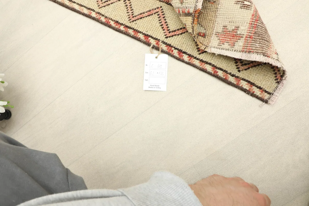 A hand holding a tag next to the folded rug, with a partial view of the rug's pattern and colors.