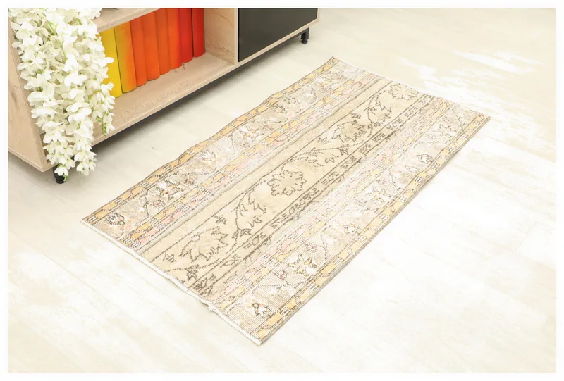 Top view of the 2'2" x 4'3" beige patchwork rug with floral and geometric motifs, laid on a white floor.