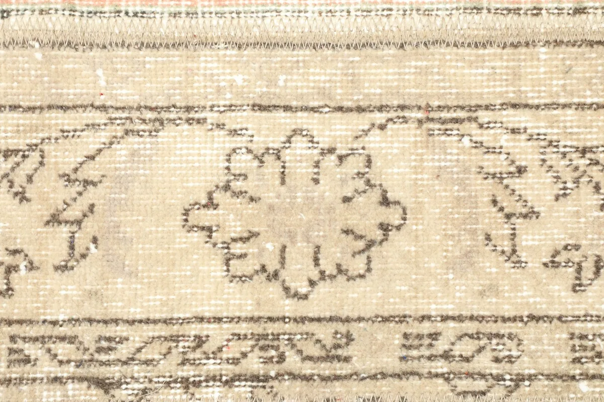 Detailed view of a stylized floral motif and border elements in shades of beige and brown.