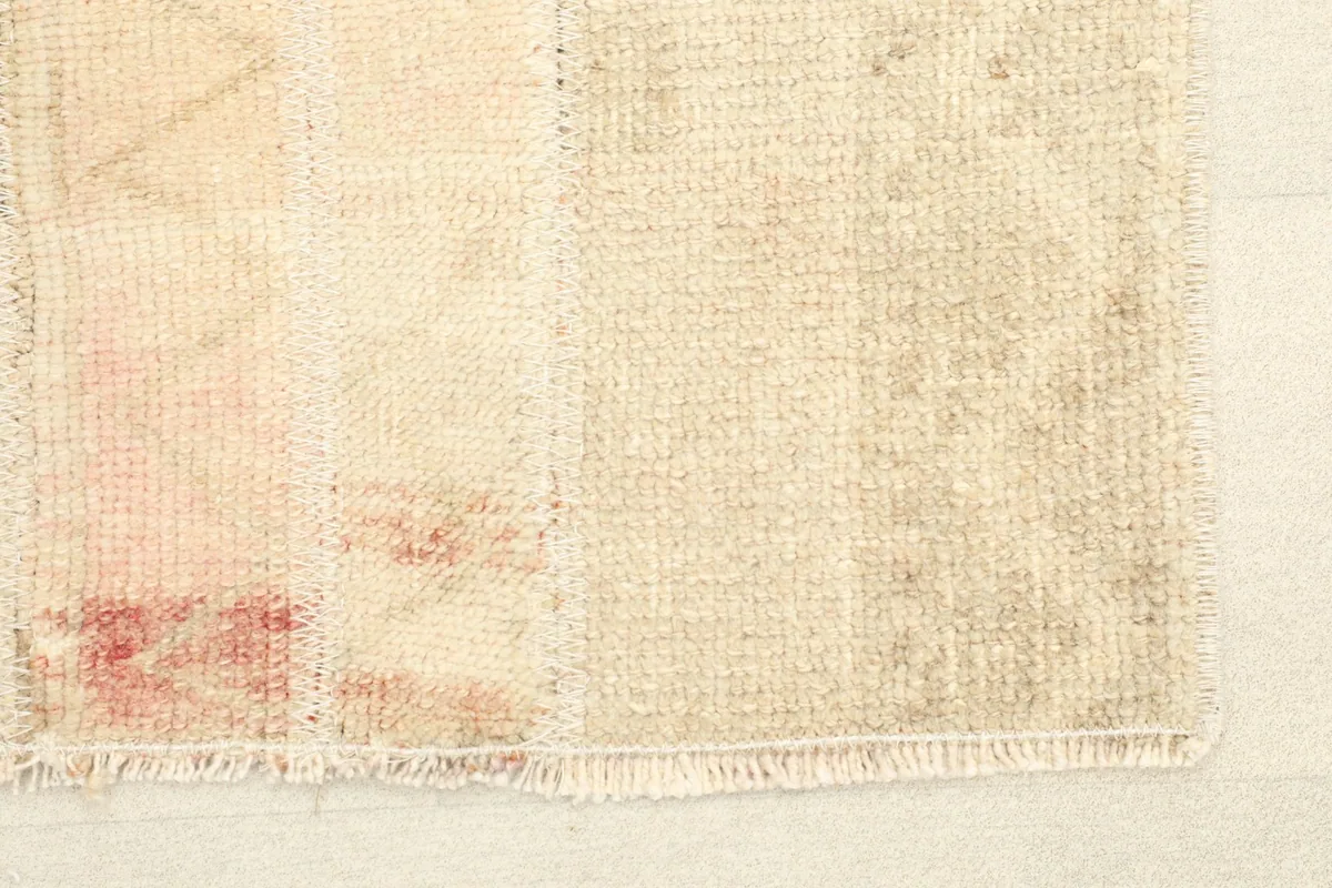 Close-up of the rug's end, highlighting the hand-knotted wool pile, cotton foundation, and subtle rose tones.