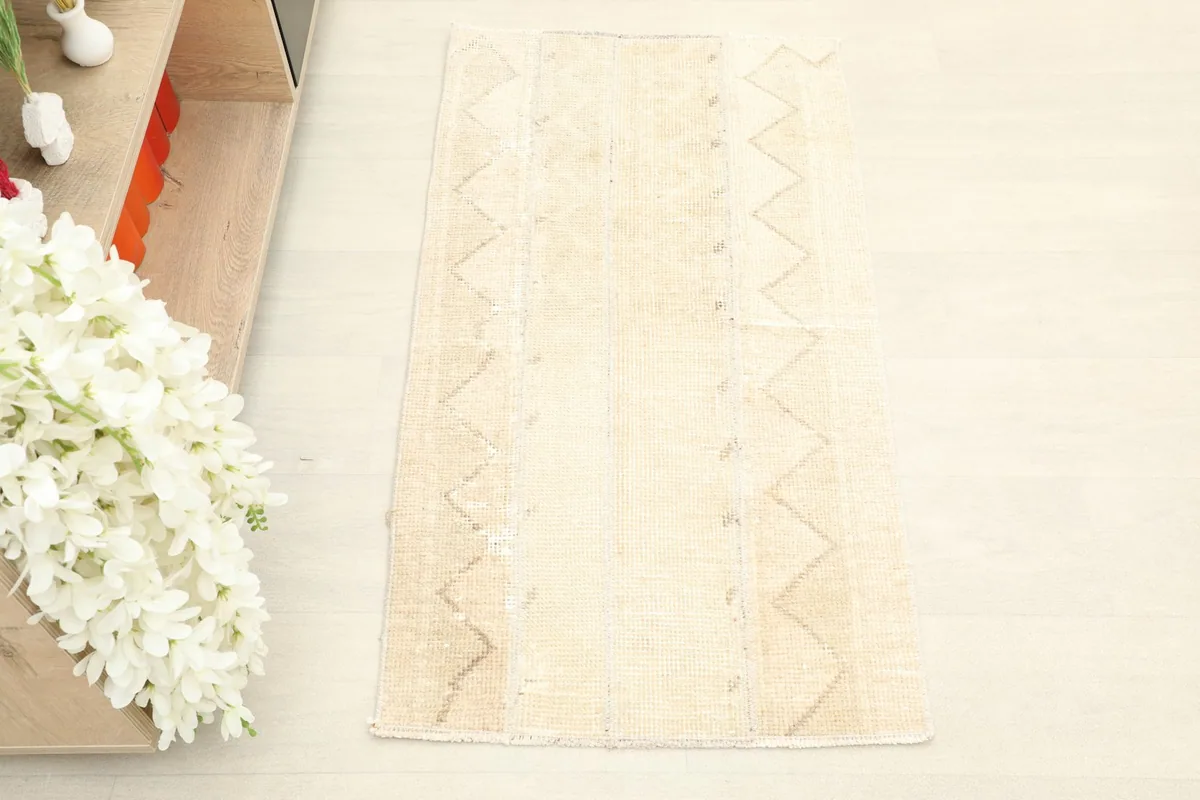 Overhead shot of the small hand-knotted wool rug, showcasing its light ivory field and faint tan patterns.