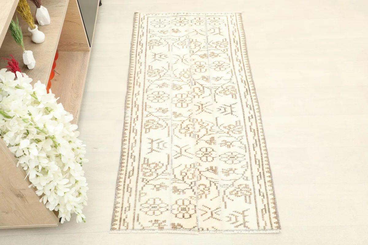 Overhead view of the ivory and tan vintage rug placed in a room setting on a light floor, next to a shelf.