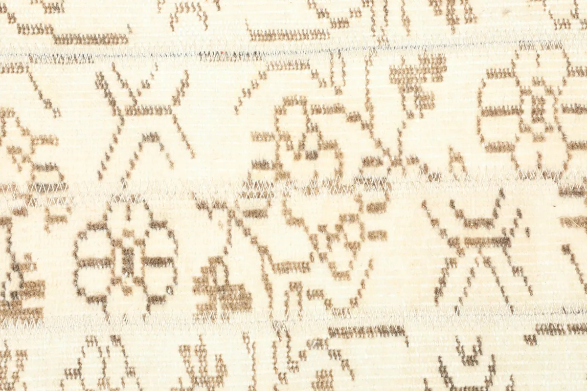 Detailed close-up of the hand-knotted wool pile, showing the texture and tan patterns on the ivory background.