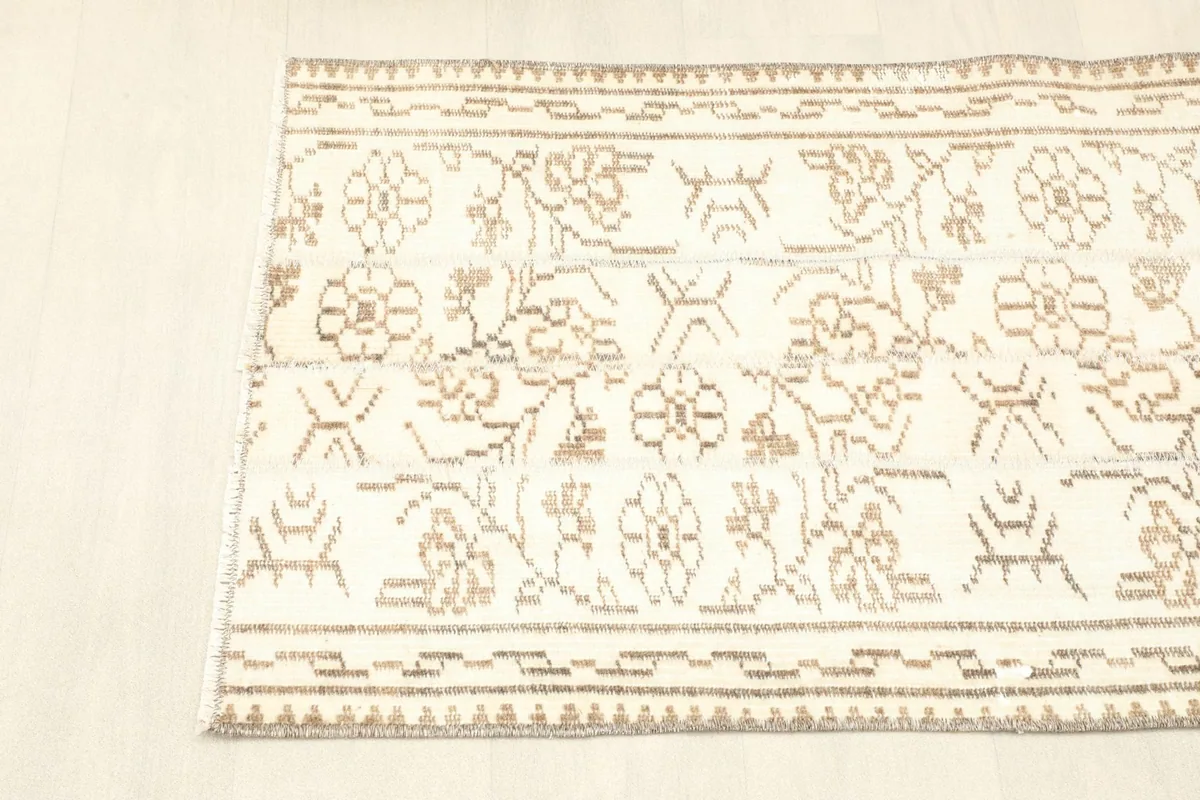 View of one end of the rug, highlighting the tan border design and central ivory field with floral patterns.