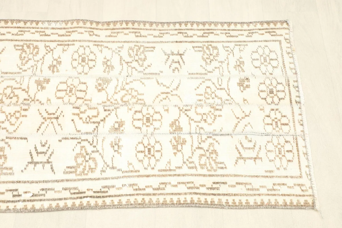 View of the opposite end of the rug, showing the consistent tan border and ivory field with patterns.