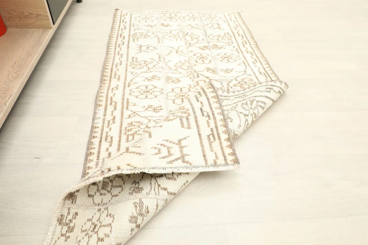 The vintage rug partially folded, displaying both the top pile and the underside, indicating flexibility.