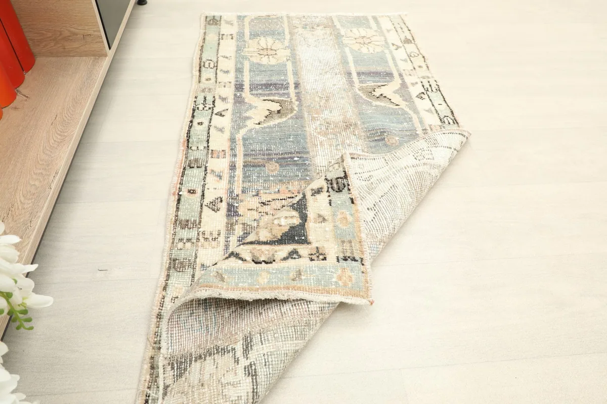 Rug partially folded, displaying the back of the hand-knotted structure and the distressed front.