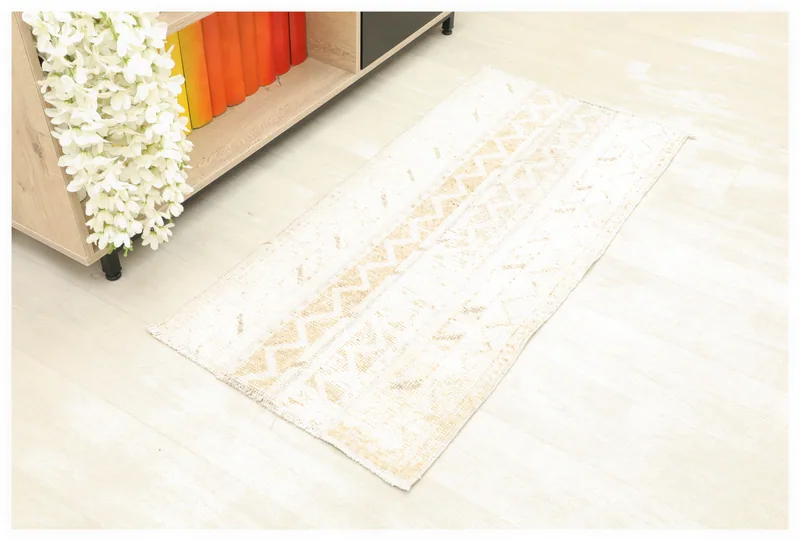 Full top view of the ivory and beige vintage Anatolian rug on a white background, next to a shelf.