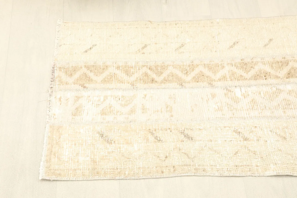Angled view of one end of the rug, displaying the ivory and beige patterns and fringe.