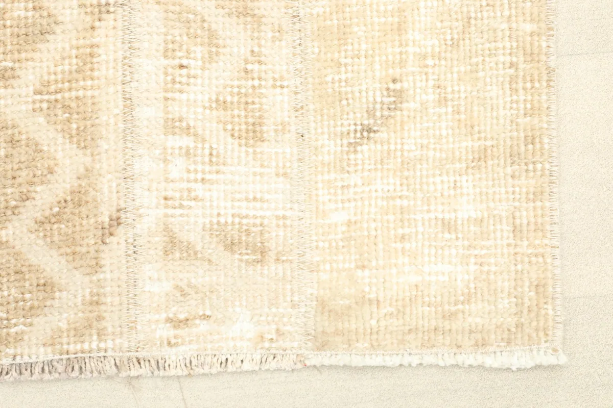 Close-up detail of the rug's texture and subtle beige geometric patterns on the ivory field.
