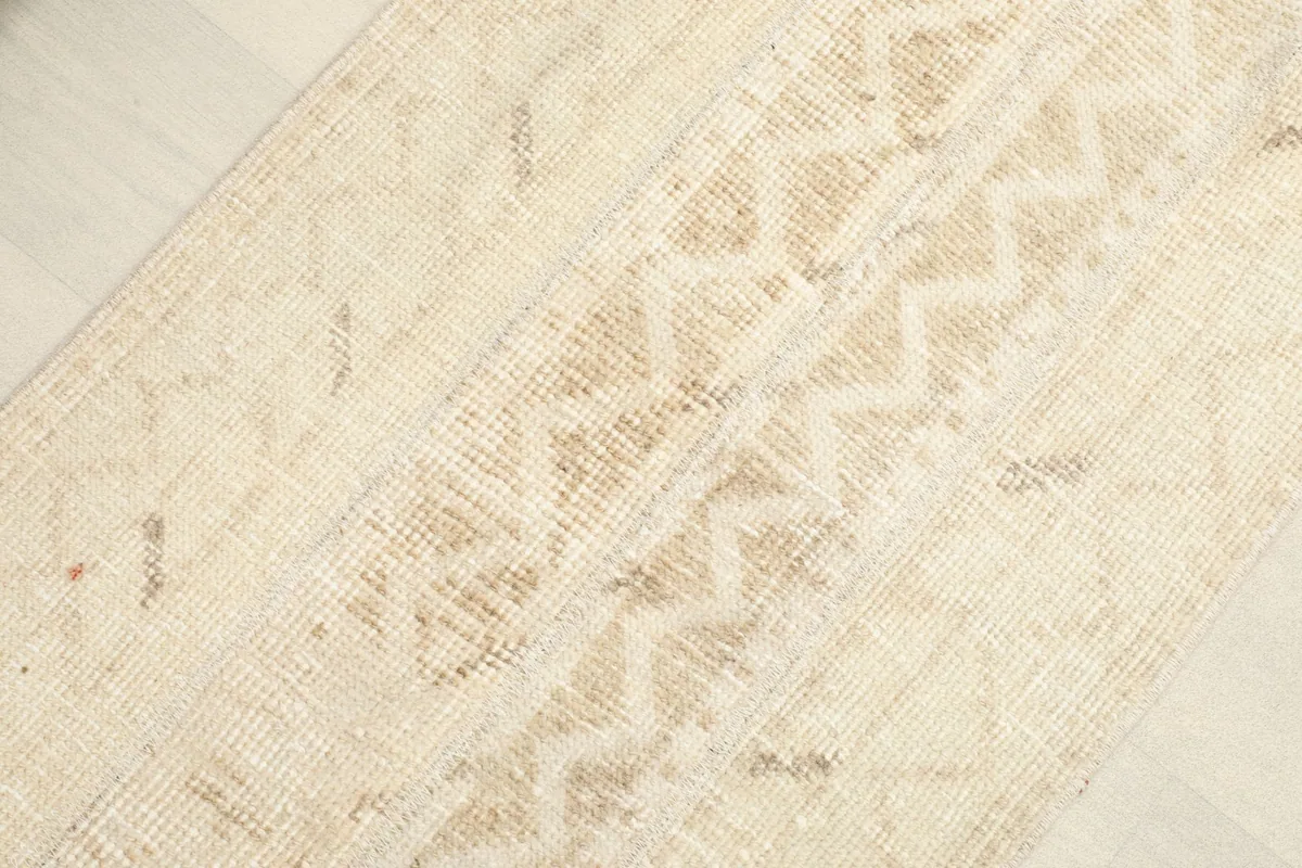 Angled close-up of the rug's surface, highlighting the faded geometric motifs in tan and beige.