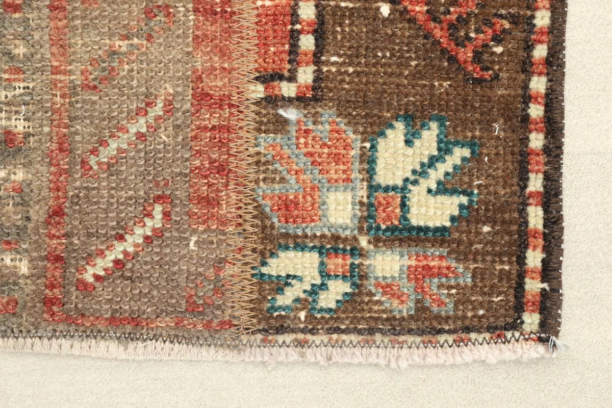 Close-up detail of the rug's corner, showing brown border, beige field, and blue, rose, ivory geometric patterns.