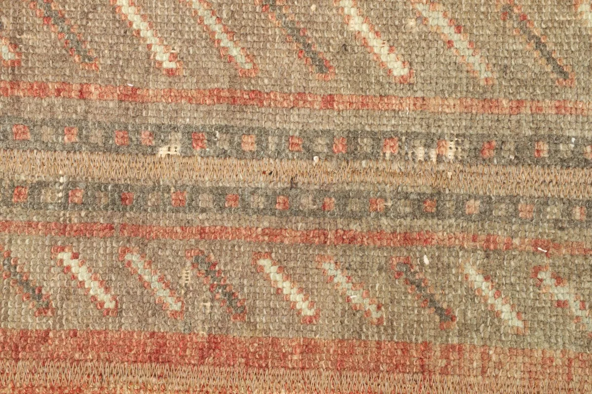 Detailed view of the rug's central field with beige, rose, and gray stripes and subtle wear.