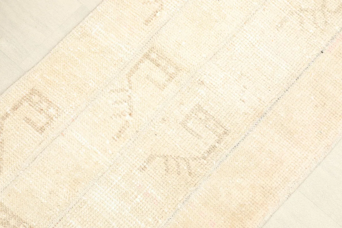 Angled view showcasing the overall texture and the faded beige geometric designs on the ivory field.