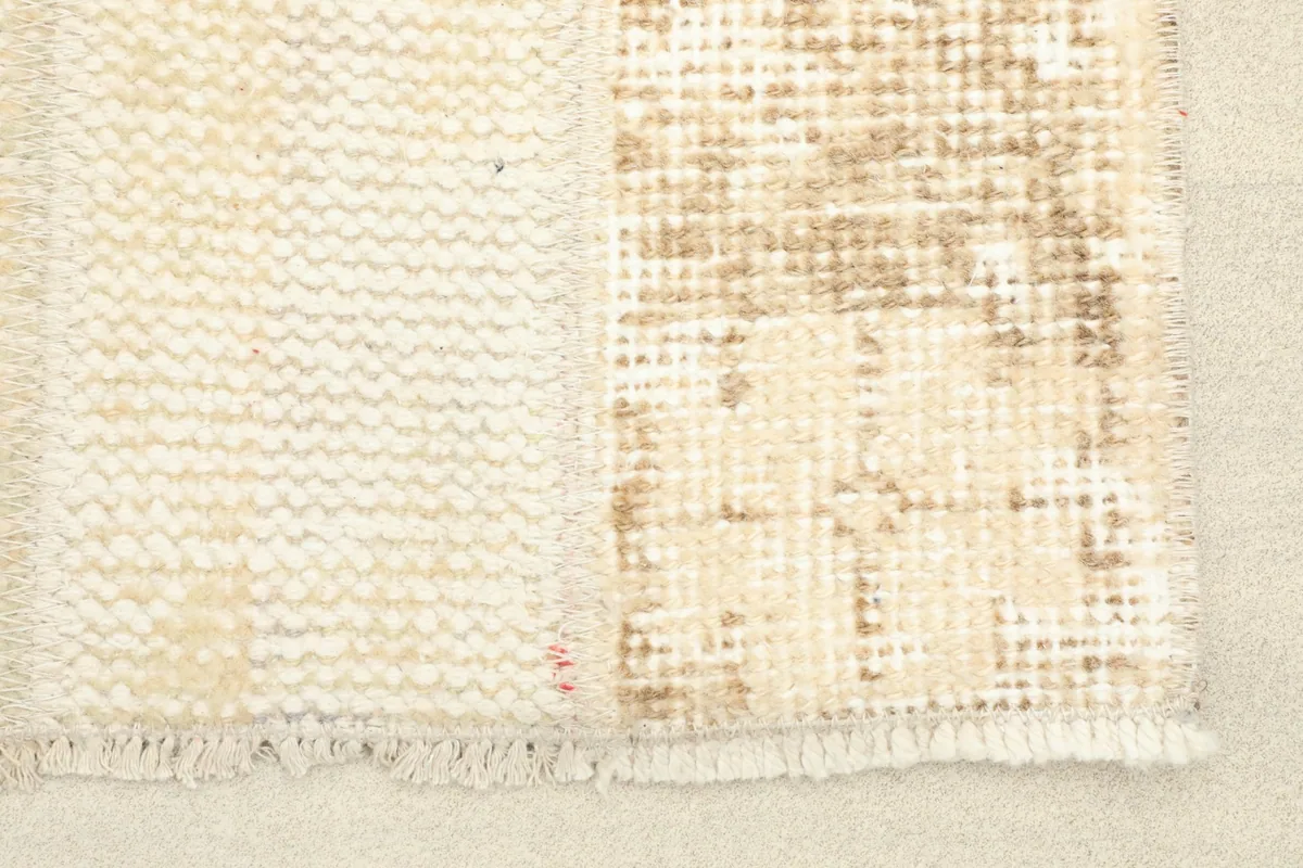 Close-up detail of the rug's distressed ivory field and tan geometric patterns, showing texture.
