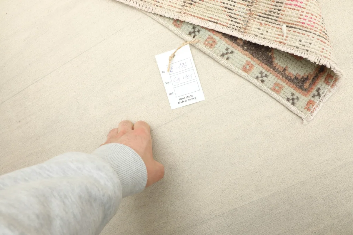 A hand next to the rug and product tag, indicating the mini size and texture of the wool.