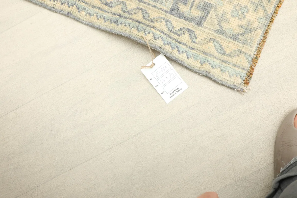 Corner of the rug with a tag, showing its size in relation to a foot