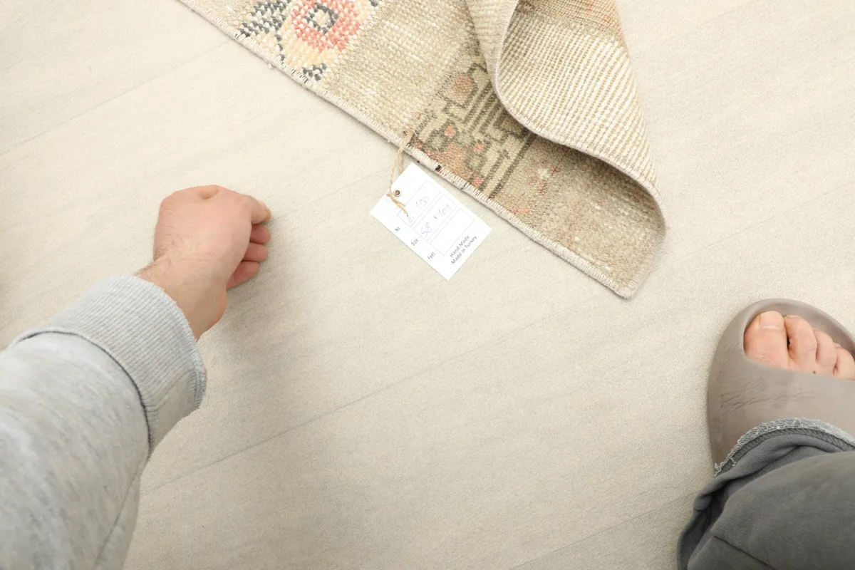 Top-down view of a hand next to the rug, showing its small size and a product tag.