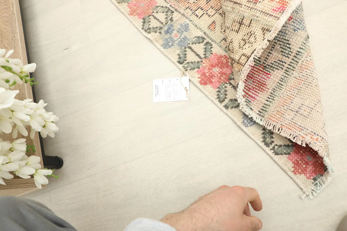 Hand pointing to the rug, showing its small scale and the texture of the low pile.