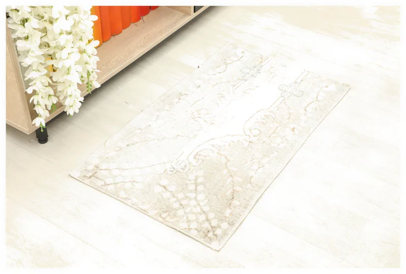 Full overhead view of the beige and ivory vintage Anatolian rug on a white floor next to a bookshelf.