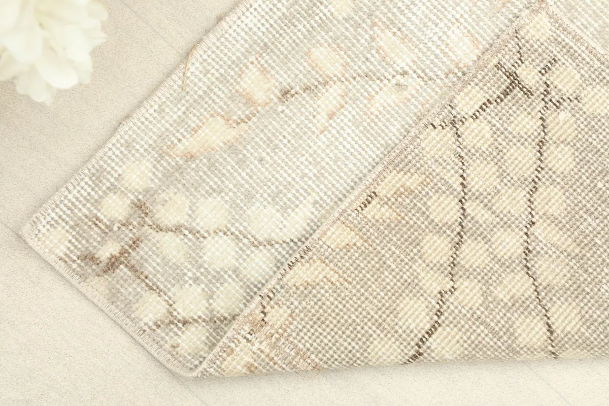 Corner of the rug folded back, showing the cotton foundation and the reverse side of the knots.