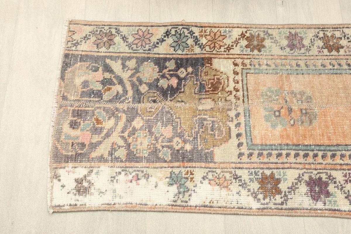 Detail of the rug's end, showing the navy and beige border patterns and the faded orange field.