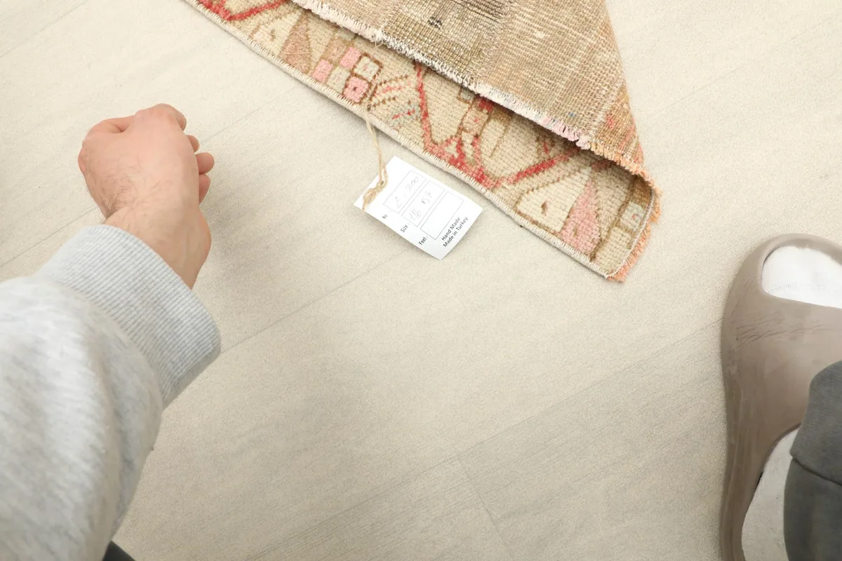 Hand pointing to the rug's back, showing the tag and illustrating the rug's mini size.