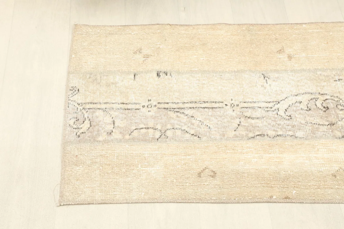 Angled shot of the rug's upper section, showing the beige field and part of the gray design.