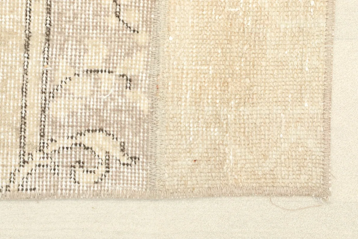 Close-up detail of the rug's edge, showing the beige field and faded gray pattern.