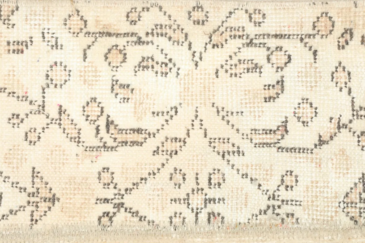Detail of a geometric pattern section within the beige patchwork rug, showing subtle wear.