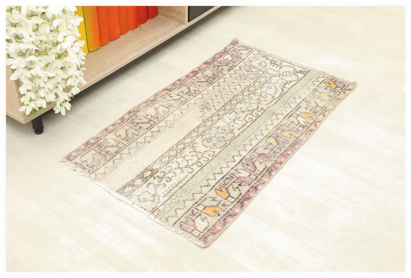 Full top view of the 1'10" x 3'3" ivory vintage Anatolian rug on a light floor, next to a shelf with white flowers