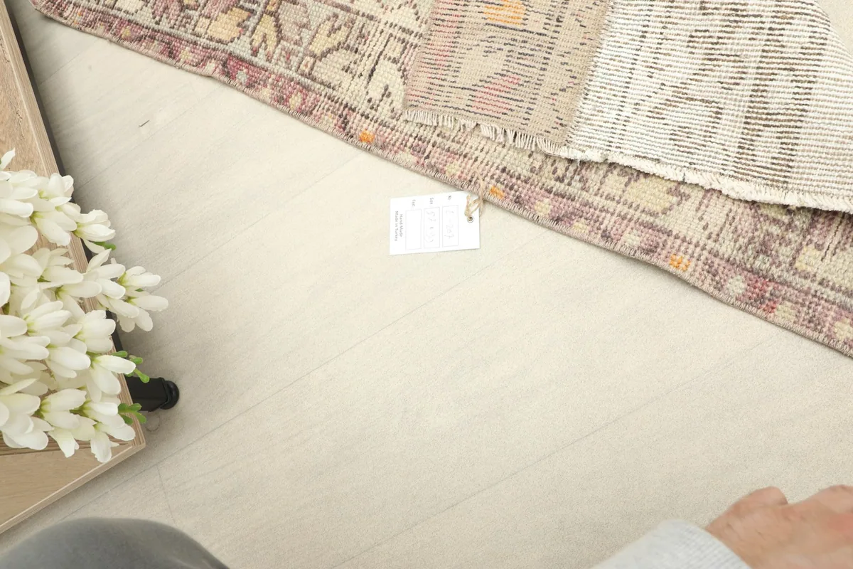 Top-down view showing the rug's texture and a tag on the floor, with flowers in the corner