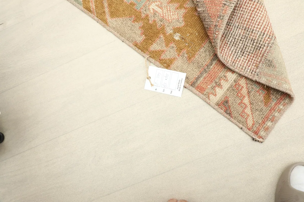 Overhead view of the rug with a tag, showing its texture and vintage character on a light floor