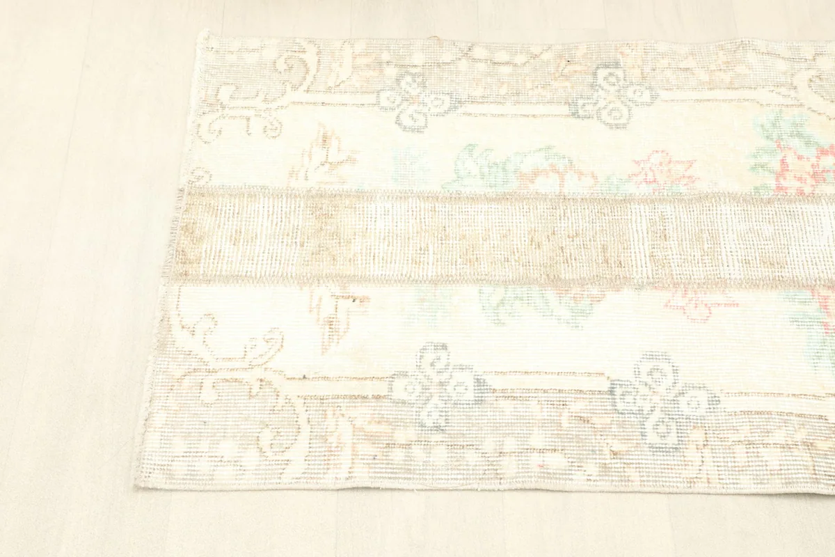 Angled view of the rug, showcasing its rectangular shape and the blend of ivory, beige, and soft colors.