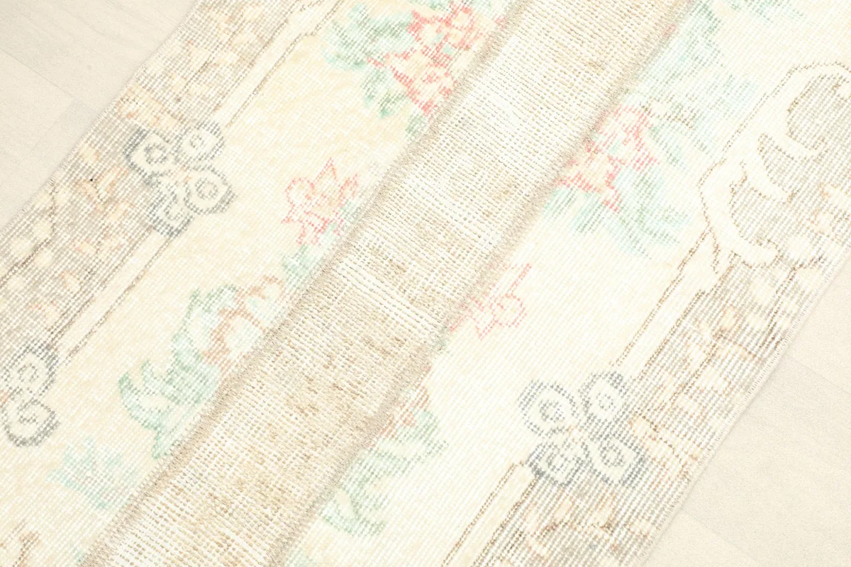 Angled close-up showing the low pile texture and faded rose, green, and blue colors within the floral motifs.