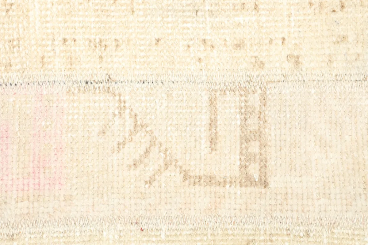 Detailed view of a geometric tribal motif in tan and a hint of faded pink on the rug