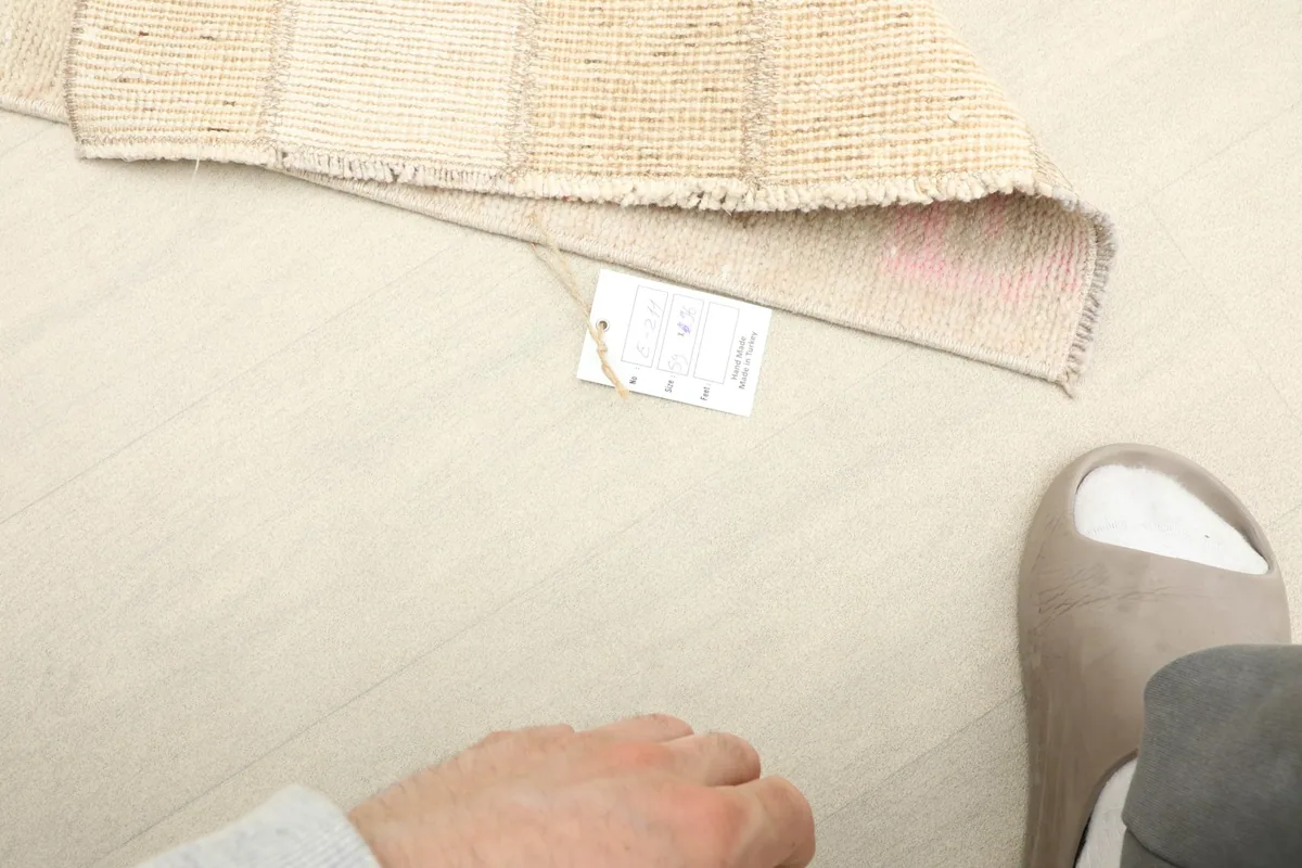View of the rug with a hand and foot for scale, showing the back and a product label