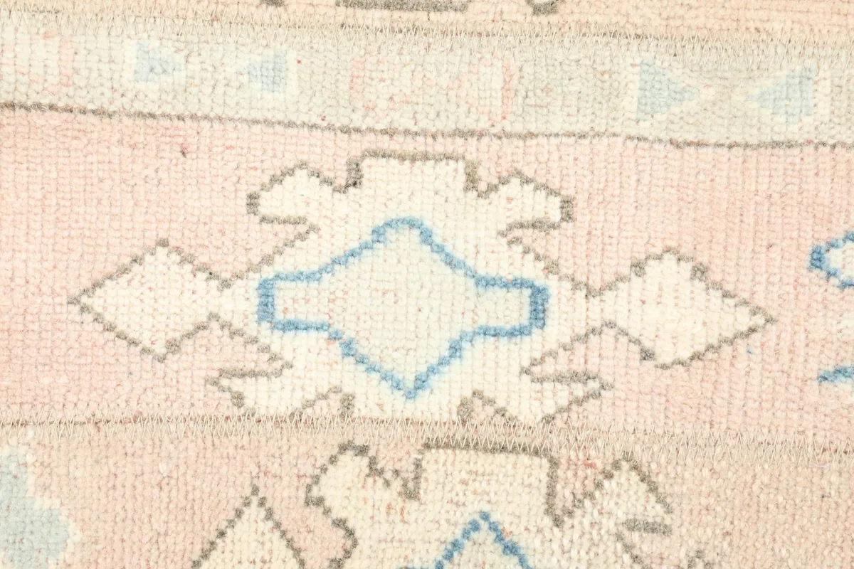Detailed view of a specific ivory and blue geometric motif within the rose field of the rug.
