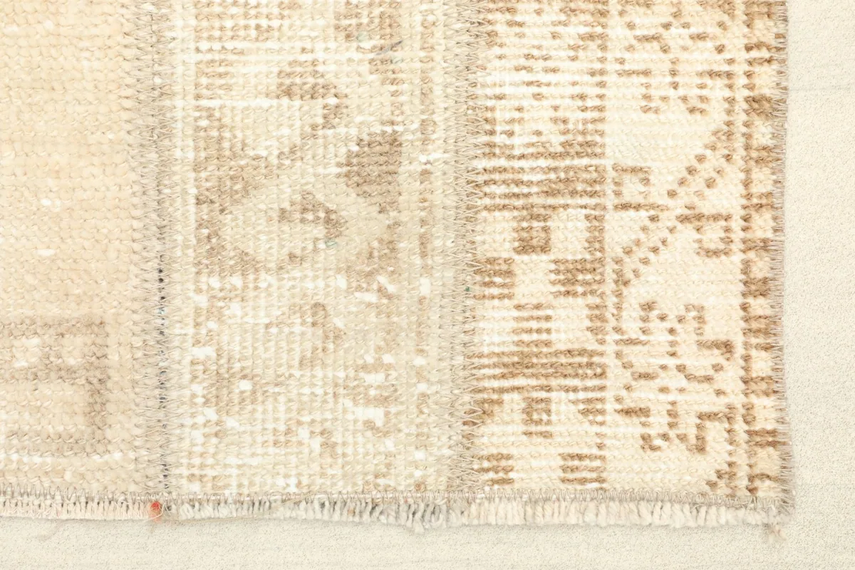 Close-up detail of the rug's edge, showing the hand-knotted texture and beige and tan geometric motifs.