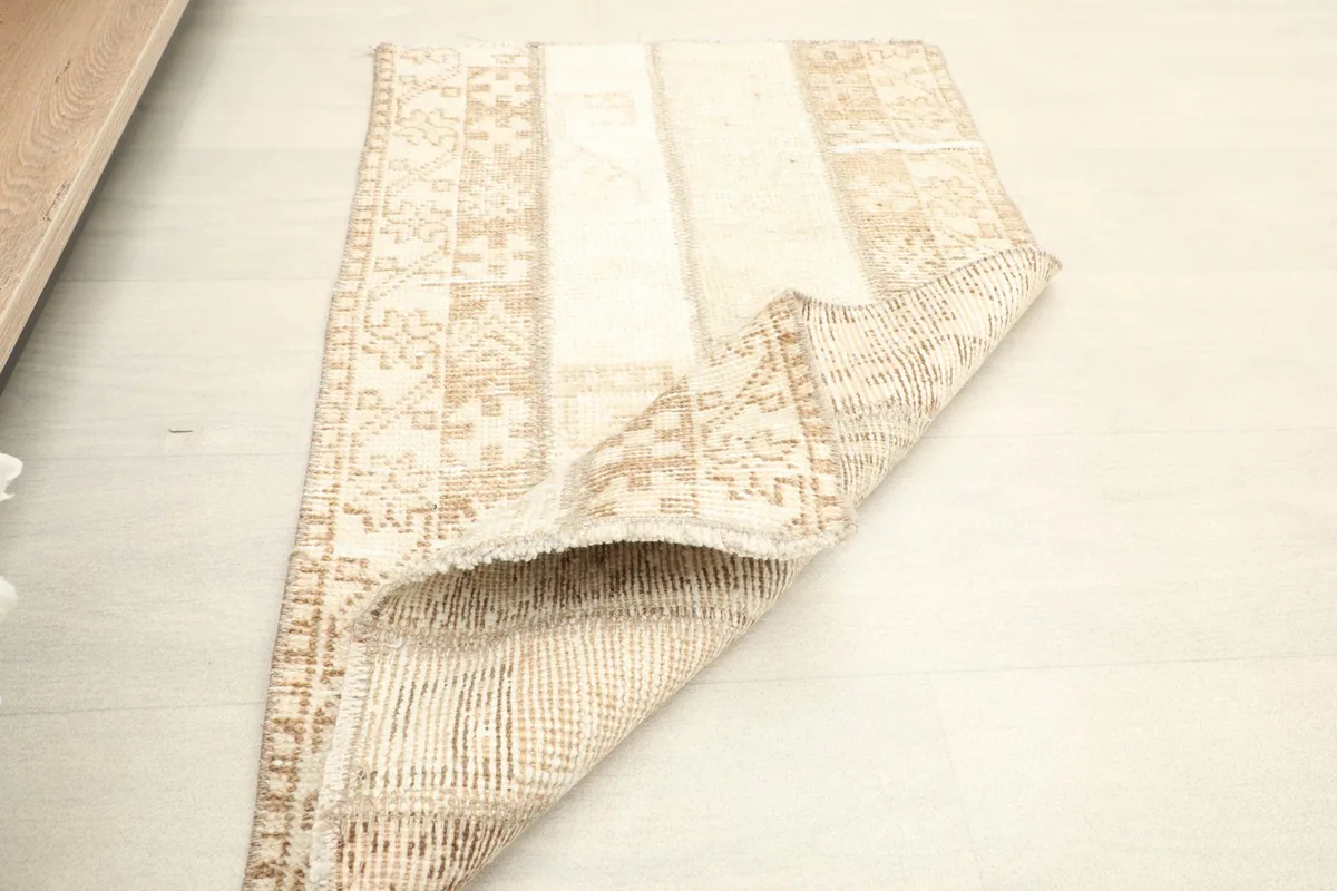 The rug partially folded, displaying both the pile side with its beige and tan patterns and the back.