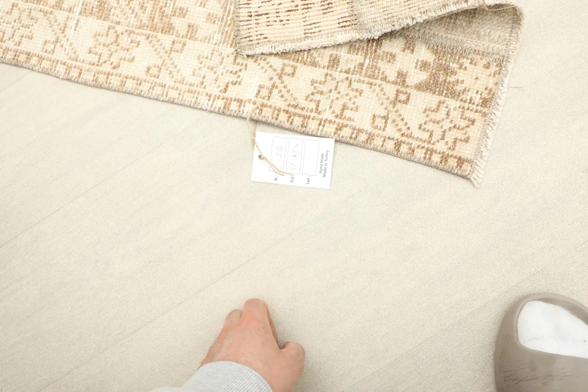 A hand next to the rug to provide a sense of scale for the 1'8" x 2'9" beige and tan area rug.