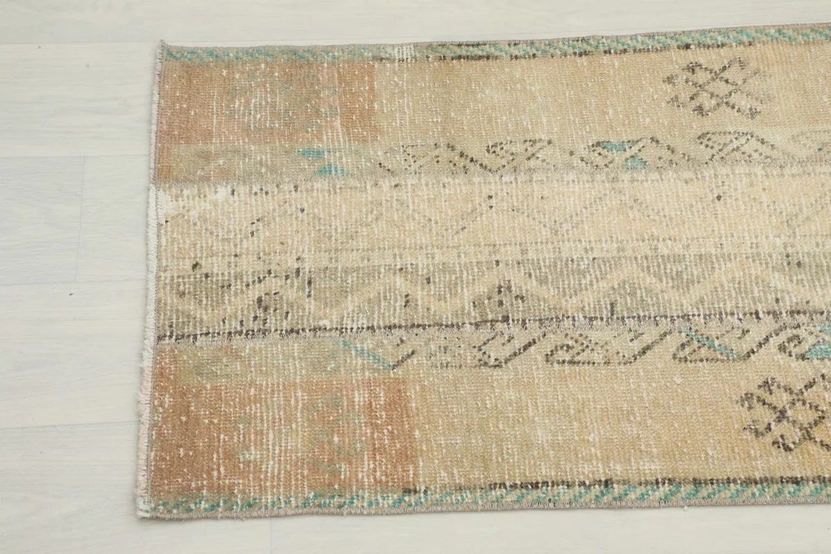 Detailed view of the rug's texture and faded beige, tan, and blue-green motifs near the edge.