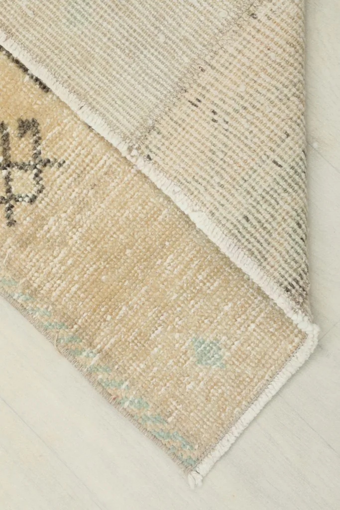 View of the rug's underside, showing the cotton foundation and reversed pile in a corner.
