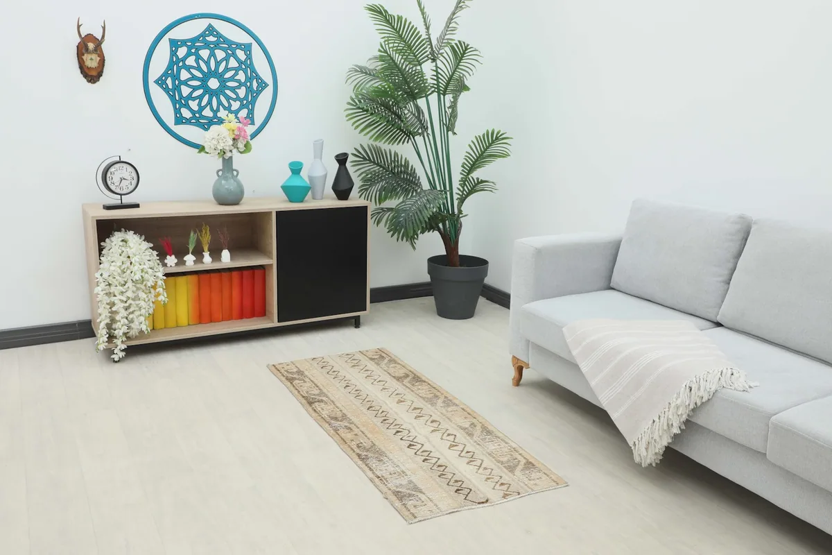 Vintage beige and brown Anatolian rug placed in a living room setting under a small sofa and cabinet.
