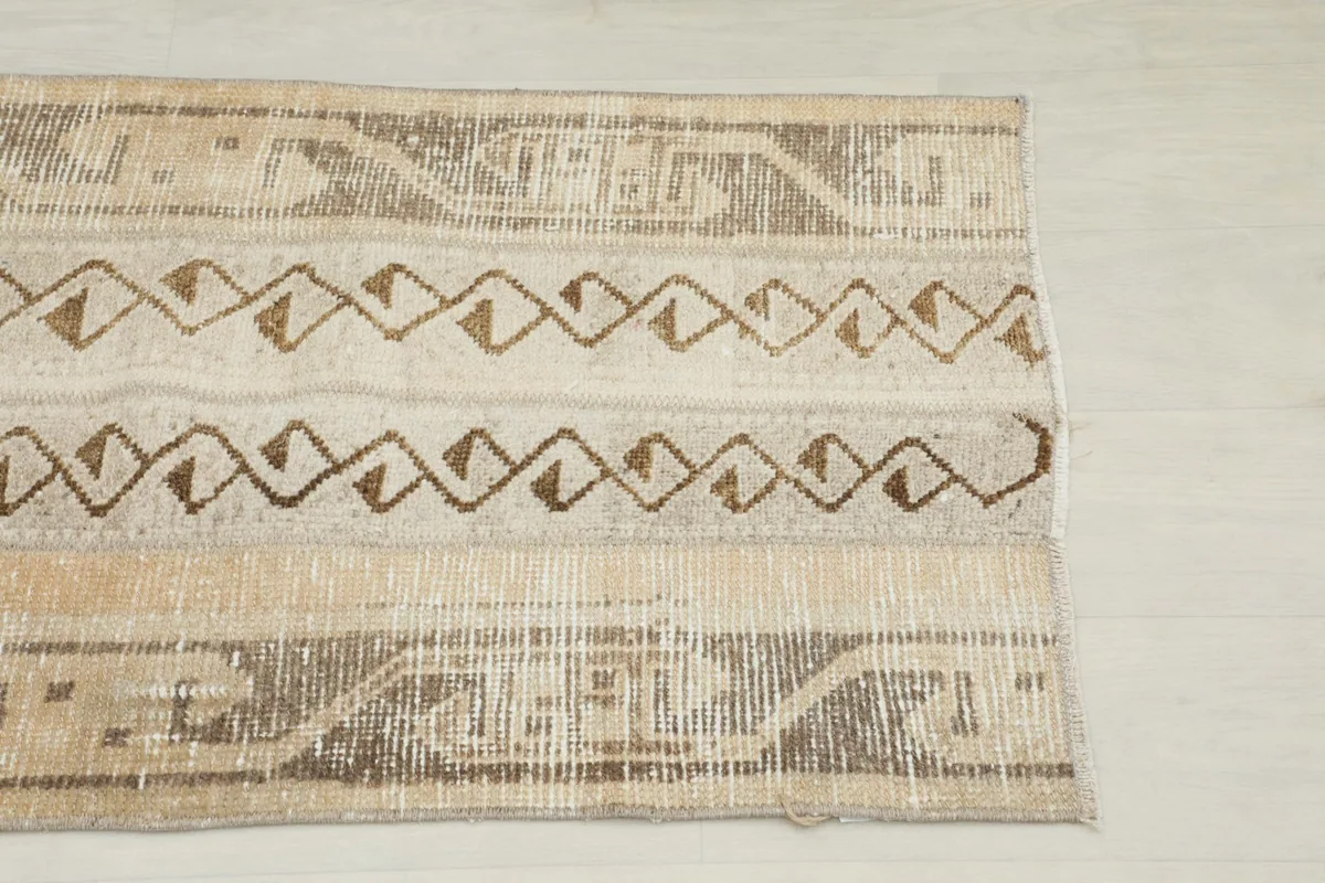 Close-up detail of the rug's end, showing the brown tribal geometric patterns against the beige background.