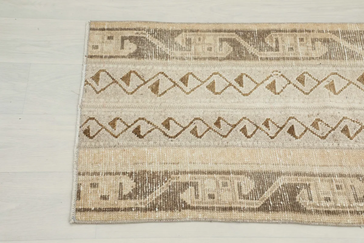 Detailed view of the vintage rug's patterns and colors, highlighting the blend of beige, tan, and brown.
